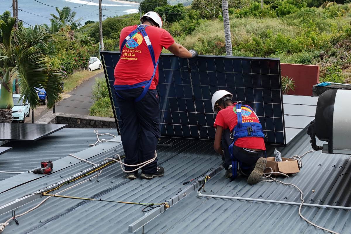 Techniciens Solar Service installant un panneau photovoltaïque sur une toiture à La Réunion avec vue littoral