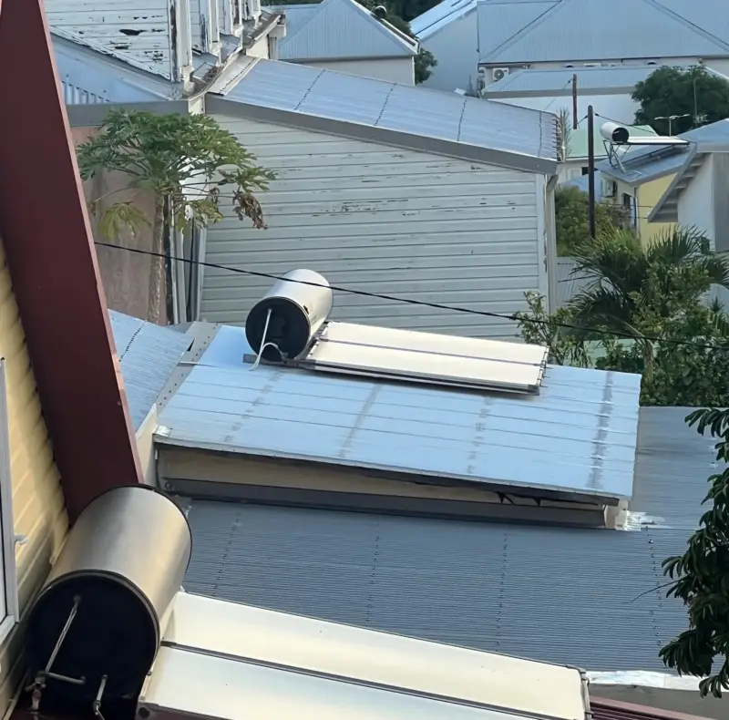 Plusieurs chauffe-eau solaires installés sur des toitures de cases réunionnaises avec vue sur l'océan