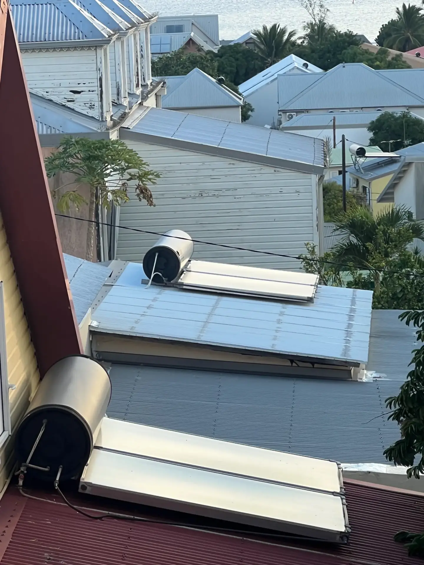 Plusieurs chauffe-eau solaires installés sur des toitures de cases réunionnaises avec vue sur l'océan