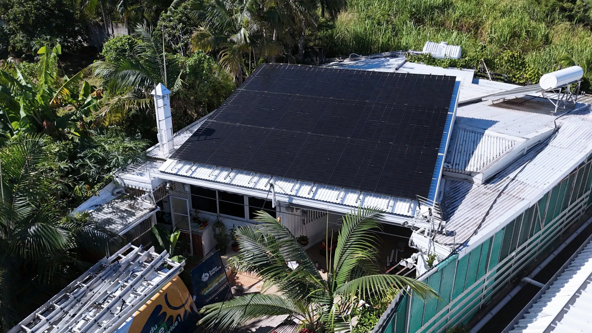 Installation photovoltaïque Solar Service 9 kWc en toiture à Petite-Île, La Réunion Vue drone de l'installation photovoltaïque Solar Service à Petite-Île, La Réunion : panneaux solaires noirs en toiture avec chauffe-eau solaire thermique