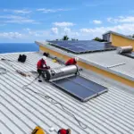 Deux techniciens Solar Service en intervention sur un chauffe-eau solaire posé sur toiture bac acier à La Réunion, vue avec l'océan en fond