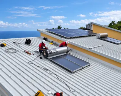 Deux techniciens Solar Service en intervention sur un chauffe-eau solaire posé sur toiture bac acier à La Réunion, vue avec l'océan en fond