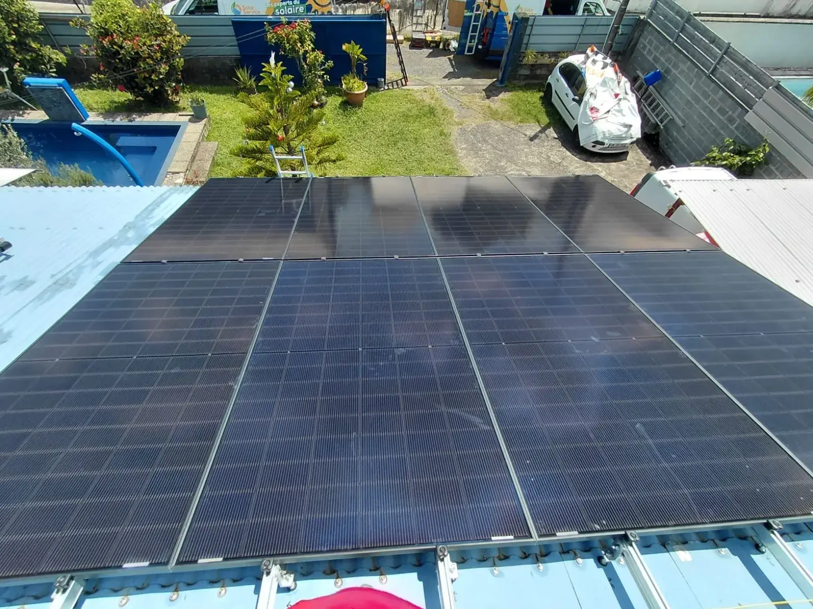 Vue aérienne d'une installation de panneaux solaires sur toiture en tôle bac acier à La Réunion, avec rails de fixation visibles et quartier réunionnais en contrebas – Solar Service